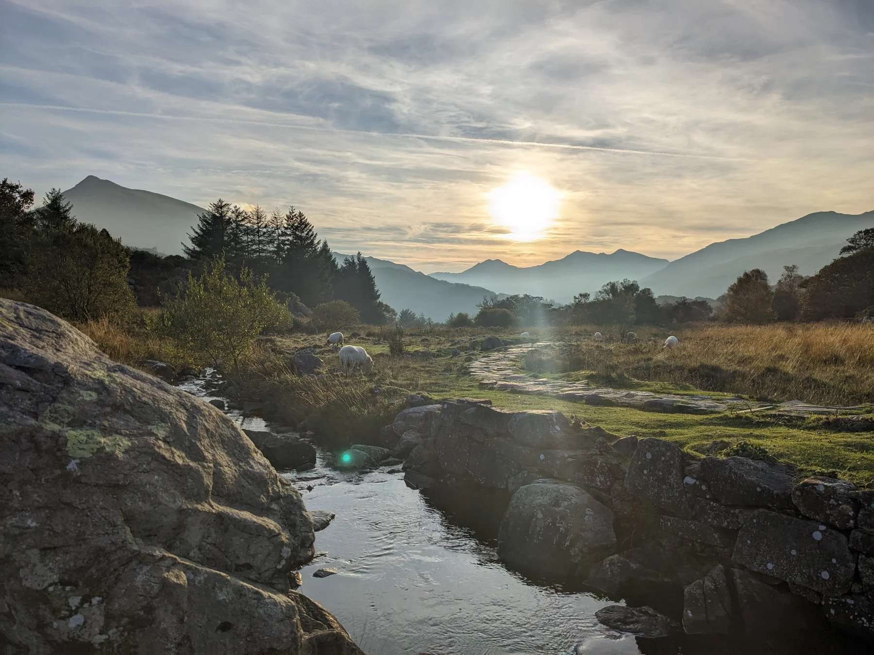 Low sunlight over layered mountain ridges and a rocky stream